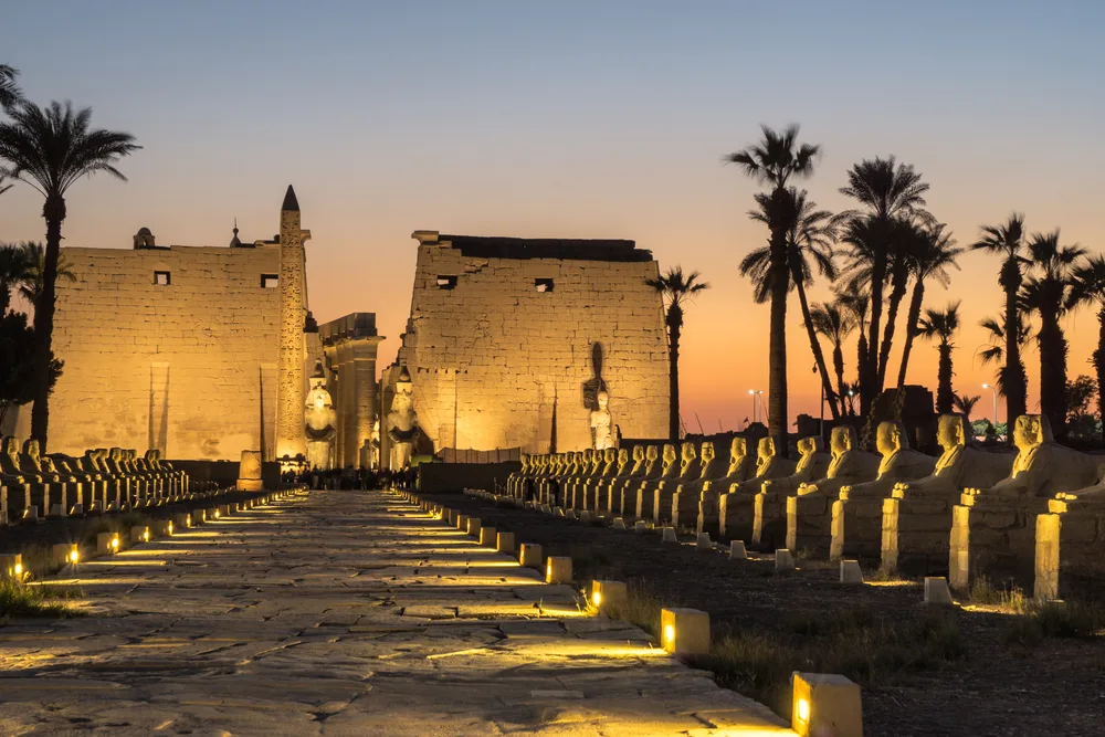 Sun setting over the Luxor Temple, one of our top picks for places to visit in Egypt, with lights illuminating the walls and sculptures outside