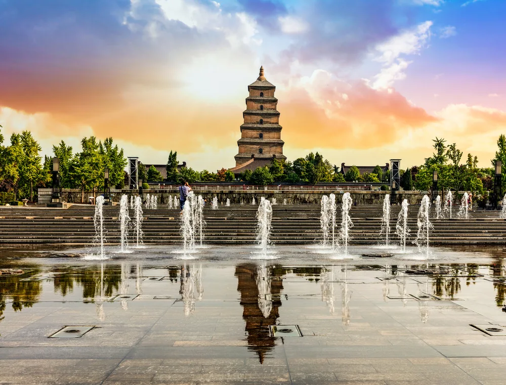 Giant Wild Goose Pagoda pictured in one of the best places to visit in China, Xian, with fountains in the foreground and a sunset in the background