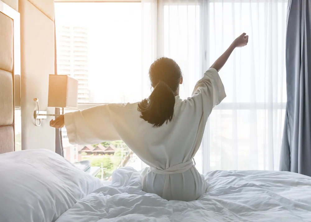 Young woman wakes up with arms outstretched on vacation to show how sleep is a health benefit of traveling