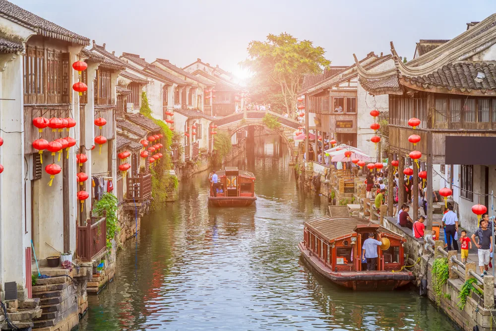 Zuzhou, dubbed "Venice of the East," pictured from above the canal looking down the water with boats making their way down the canal and bustling shops on either side