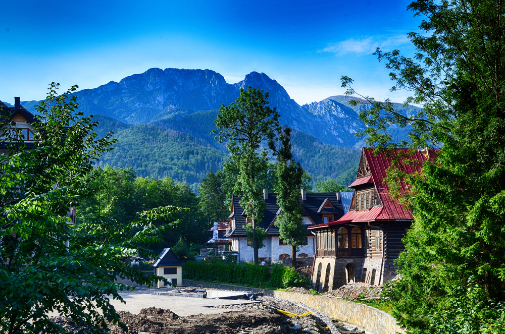 Tatra mountains and storybook homes along a water canal with a blue sky overhead for a piece on the best places to visit in Poland