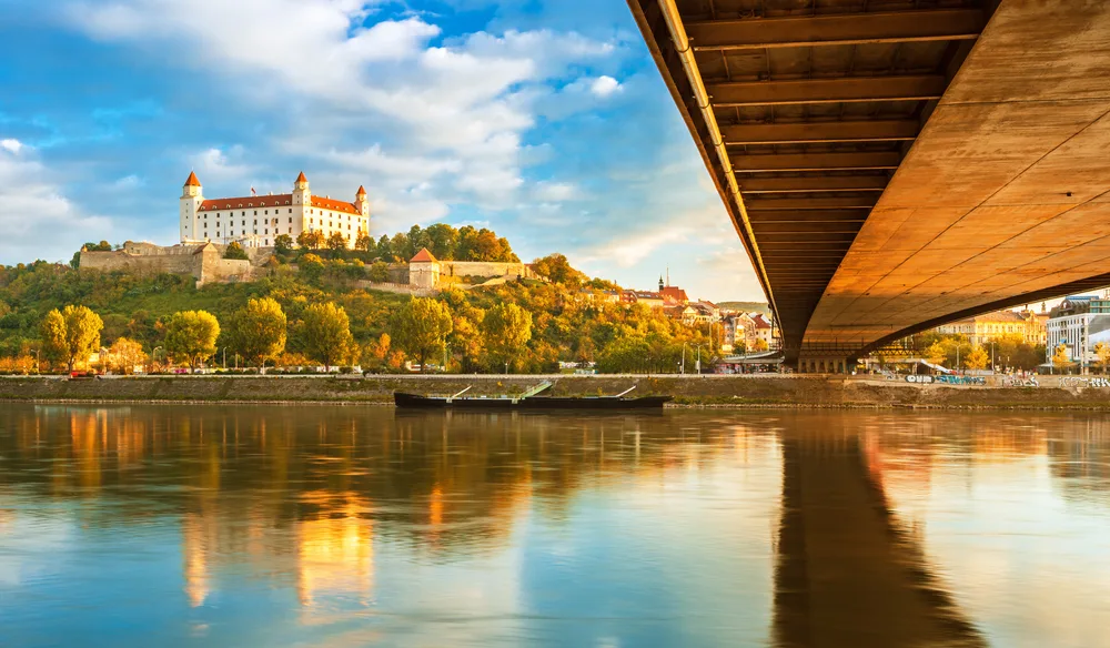 Photo of the Bratislava Castle, seen from under the wooden bridge, with still water in the river below