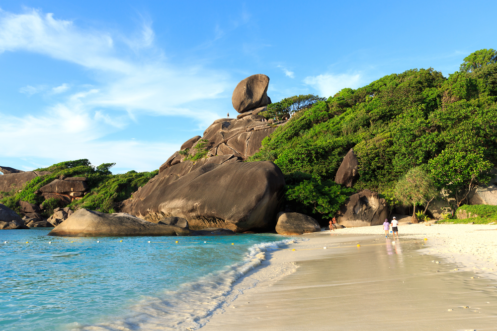Enormous rock formation towering over a couple walking along the beach in the Similan Islands, one of the best places to visit in Thailand