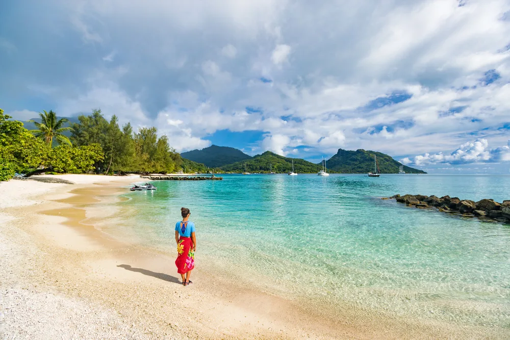 Woman in a cover-up walking along the beach in Huahine, one of our top picks for where to stay in Bora Bora