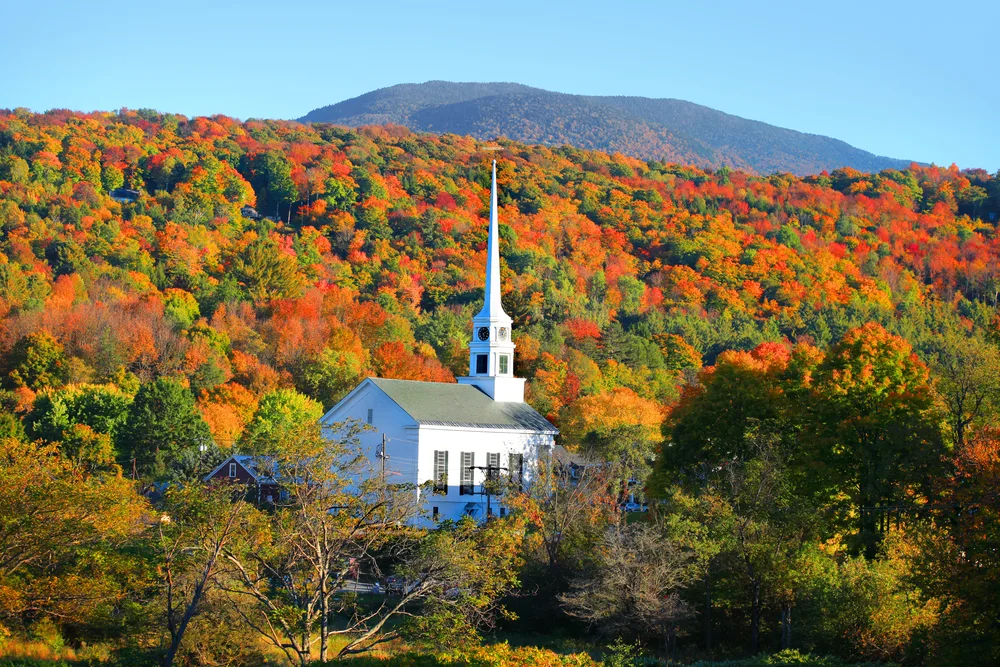 Iconic white steepled church in Stowe, Vermont, pictured in the middle of a valley with trees all around
