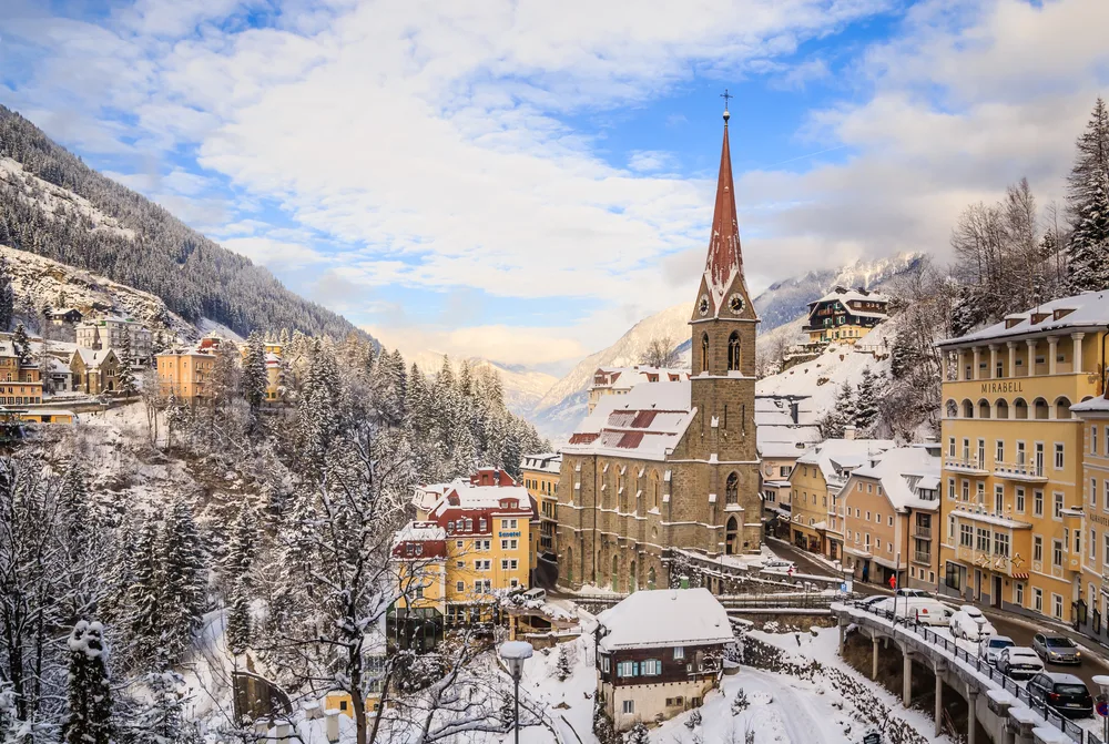 Church with a tall steeple in the middle of the charming town of Bad Gastein in Austria, featuring snow-covered mountains and roads