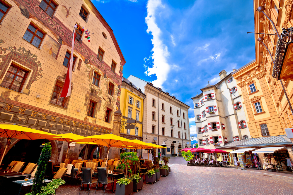 Colorful buildings in Innsbruck, one of the best places to visit in Austria, with blue skies in the background and chairs set up along the street outside of the cafes
