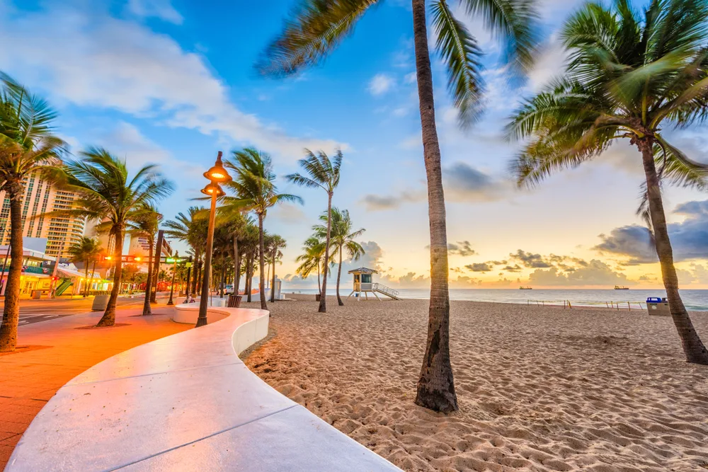 Las Olas Beach in Ft. Lauderdale at dusk with palm trees and low wall curving along the sand to show one of the best beaches in Florida