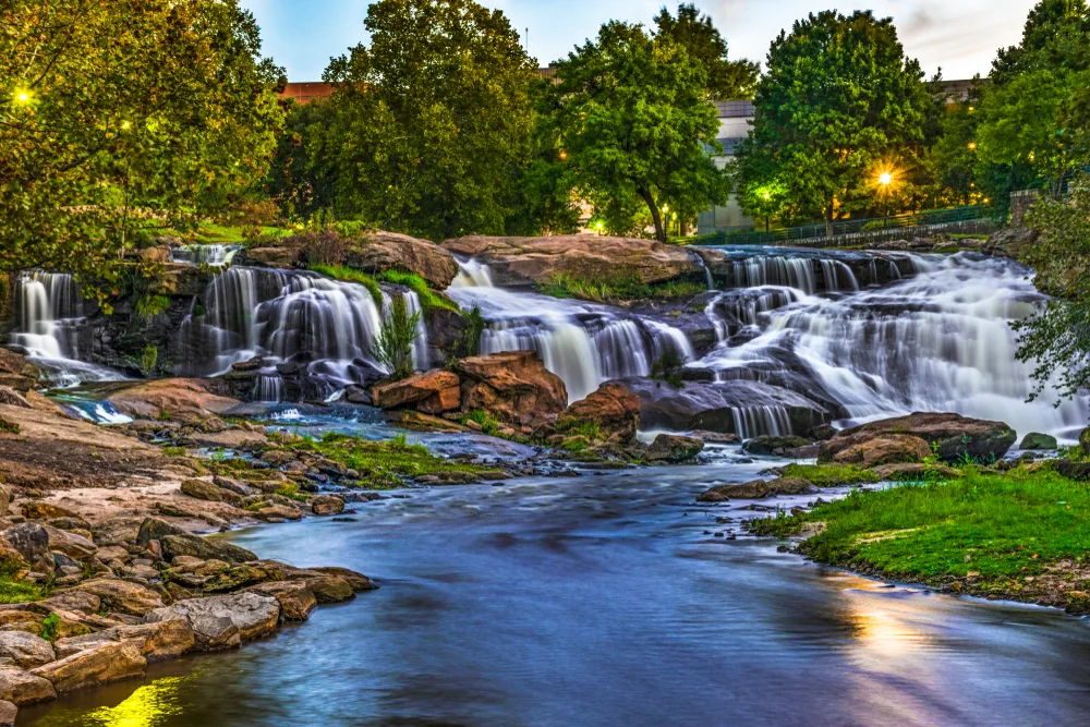 Featured as one of the best places to visit in South Carolina, a pictured of the Reedy River Falls pictured at dusk