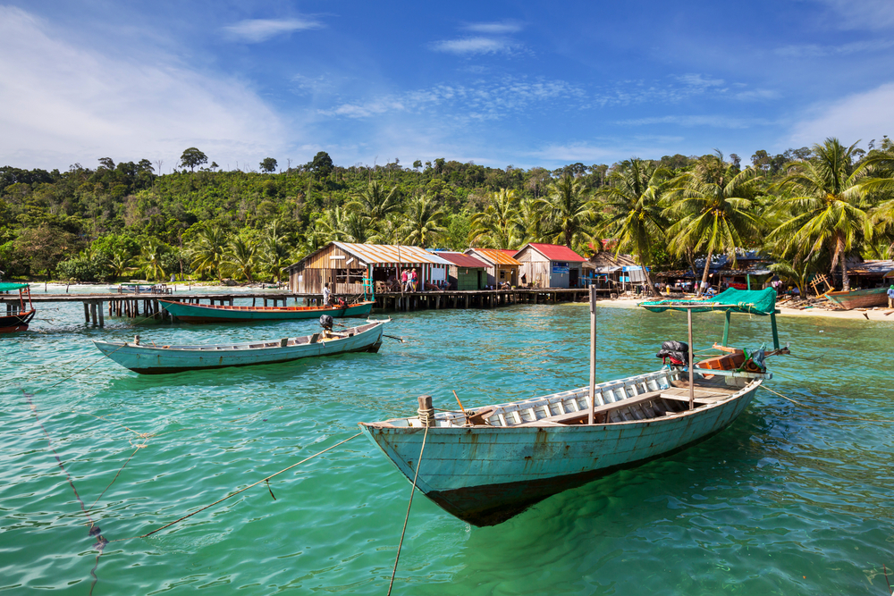 White and black fishing boats floating on the water in Kep during the best time to visit Cambodia with crystal-clear water and blue skies
