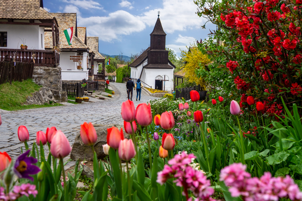 Small village of Hollókő during Easter with colorful tulips in the foreground and blue cloudy skies during the overall best time to visit Hungary