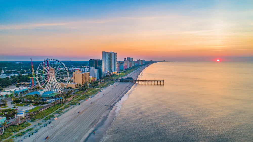 Aerial view of one of the best beaches in the US showing Myrtle Beach coastline and amusement park with a large Ferris wheel at sunset