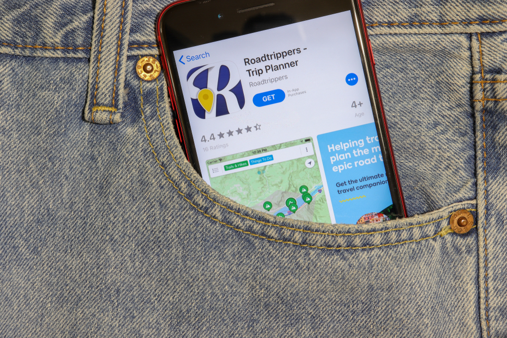 Roadtrippers is one of the greatest trip planning apps to use to plan your road trip and stops along the way, shown on a smartphone tucked into a jeans pocket