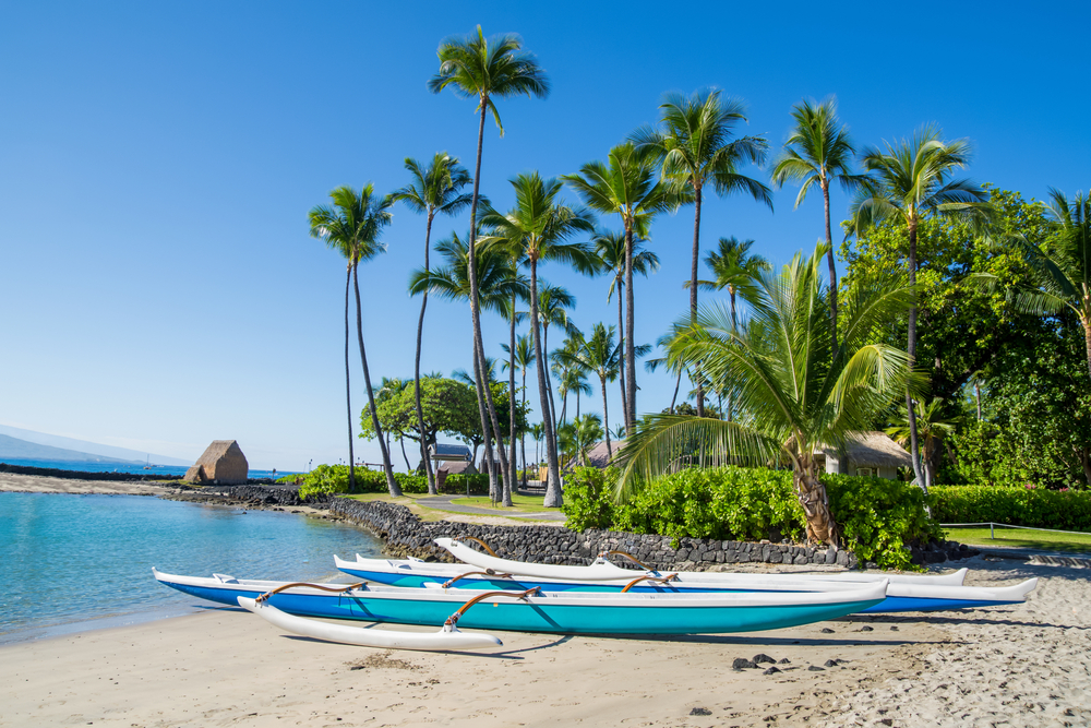 Outrigger canoe on the beach Kamakahonu Beach with palm trees in the background during the least busy time to visit Kona