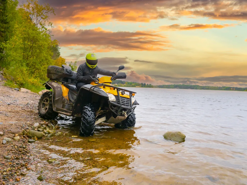 Man riding an ATV quad bike into a creek depicts the concept of visiting Winnsboro, SC for Carolina Adventure World at sunset with trails for bikes, ATVs, and hiking
