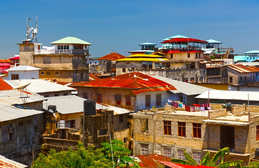 For a piece titled Is Zanzibar Safe to Visit, a bunch of run-down and colorful homes and buildings with tin roofs pictured from the top of another building