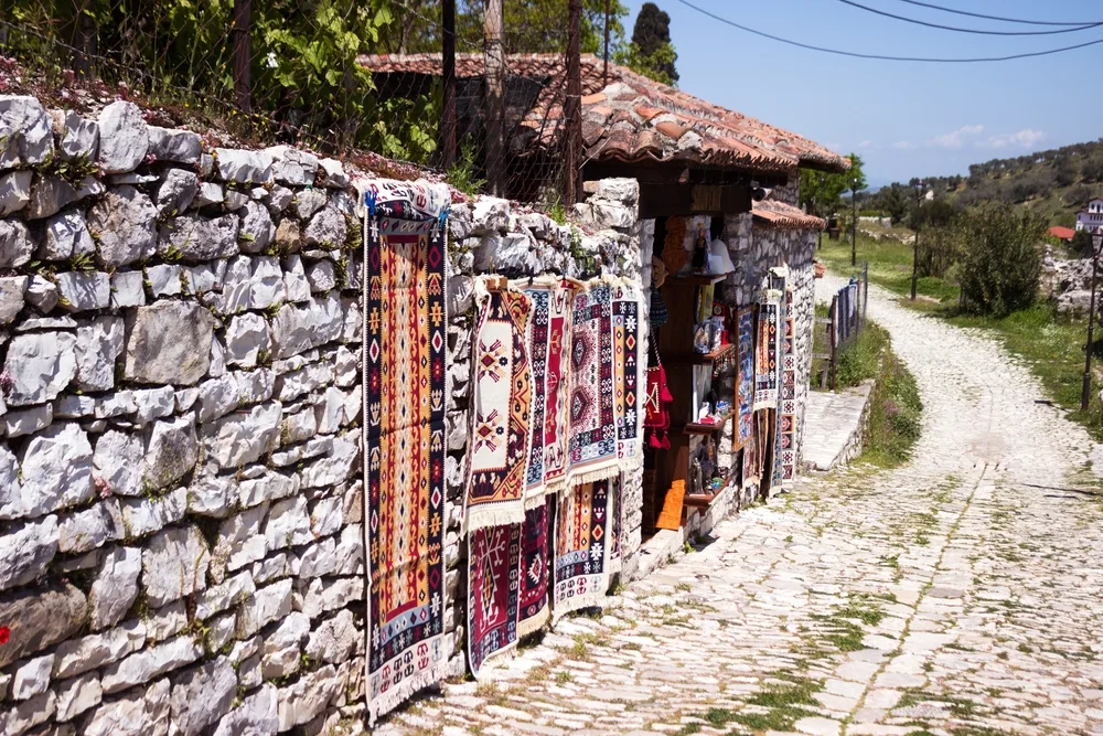 Traditional Albanian carpets hang on a stone wall for sale to show how affordable the country is to visit and shop in