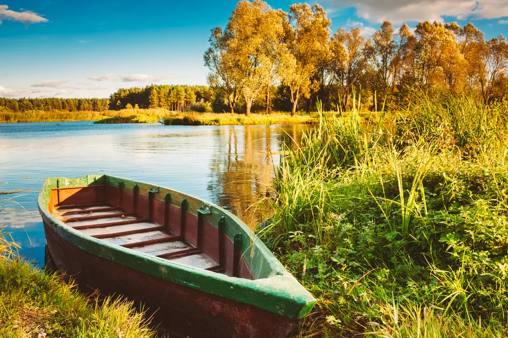 Wooden row boat on the shore of a lake during fall, showing the best time to visit Belarus with cheap prices