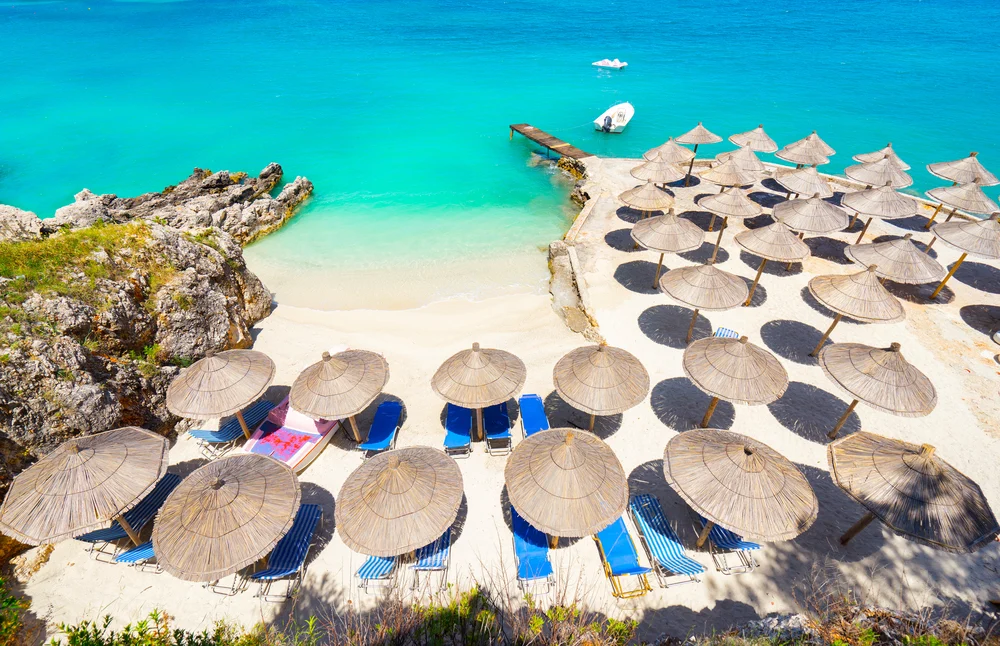 Aerial view of Ksamil Beach during the best time to visit Albania with group of thatched beach umbrellas and chairs on the sand 
