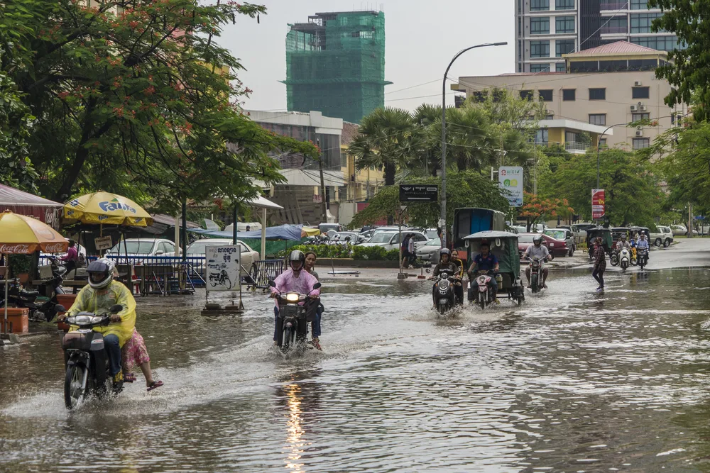 People on motorcycles and tuktuks driving through flooding and torrential rain during the worst time to visit Cambodia in the middle of the city in Phnom Penh