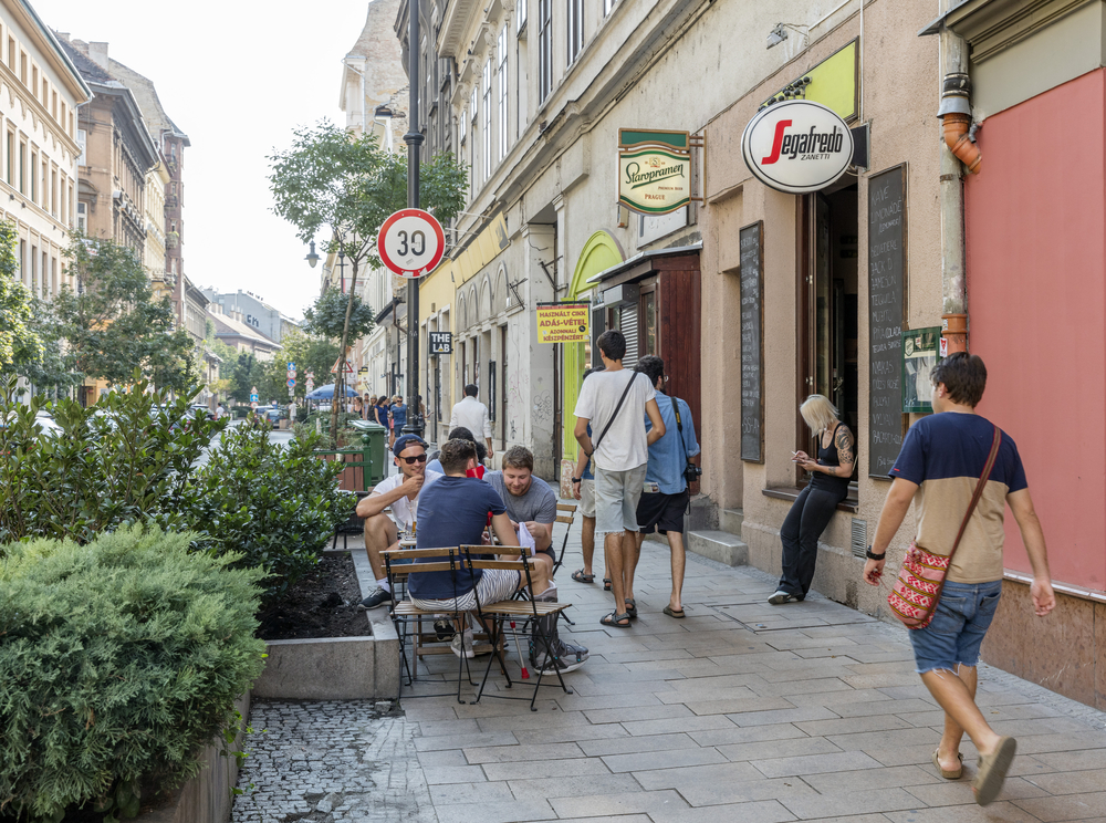 Little shops in Erzsebetvaros, one of the best places to stay in Budapest, featured with people walking by others sitting outside little cafes