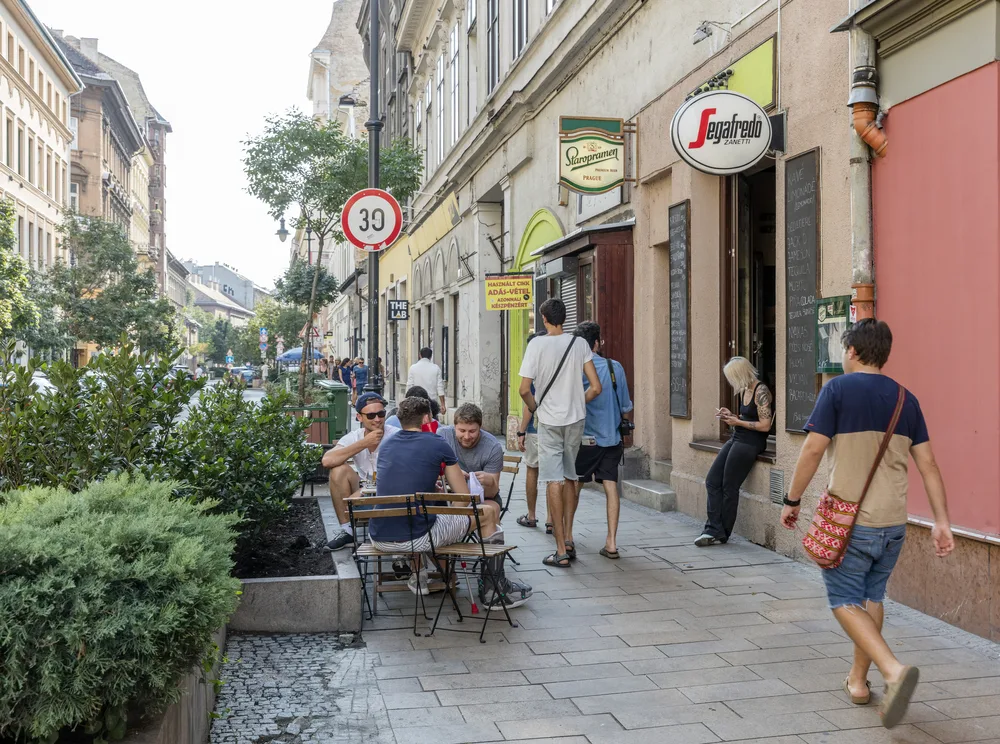 Little shops in Erzsebetvaros, one of the best places to stay in Budapest, featured with people walking by others sitting outside little cafes
