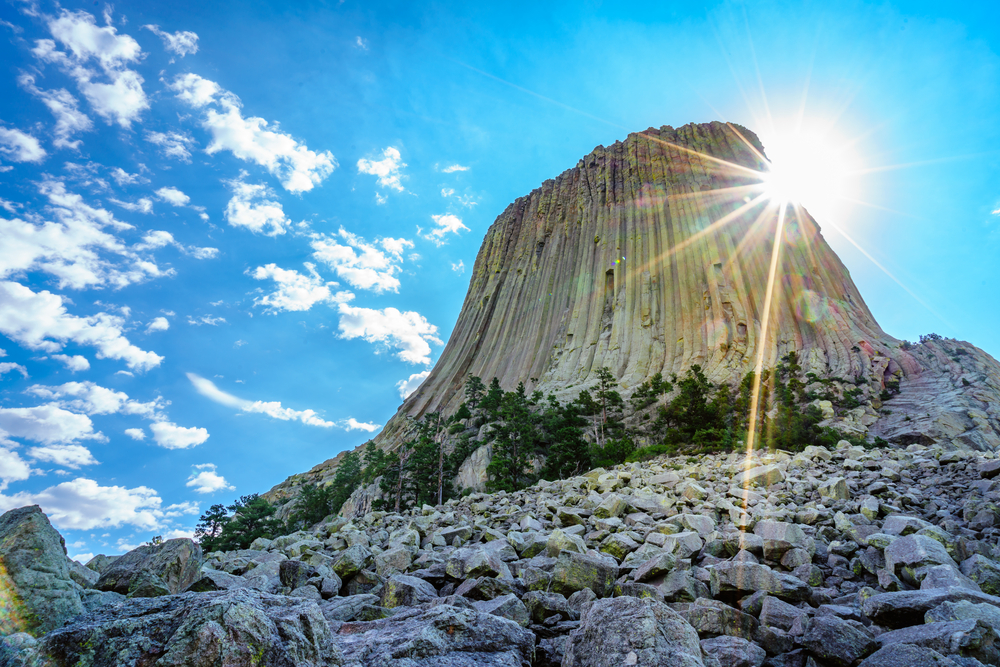 Devils tower pictured looking up toward the top with the sun shining over the rock face for a piece on the best places you have to visit on a trip to Wyoming