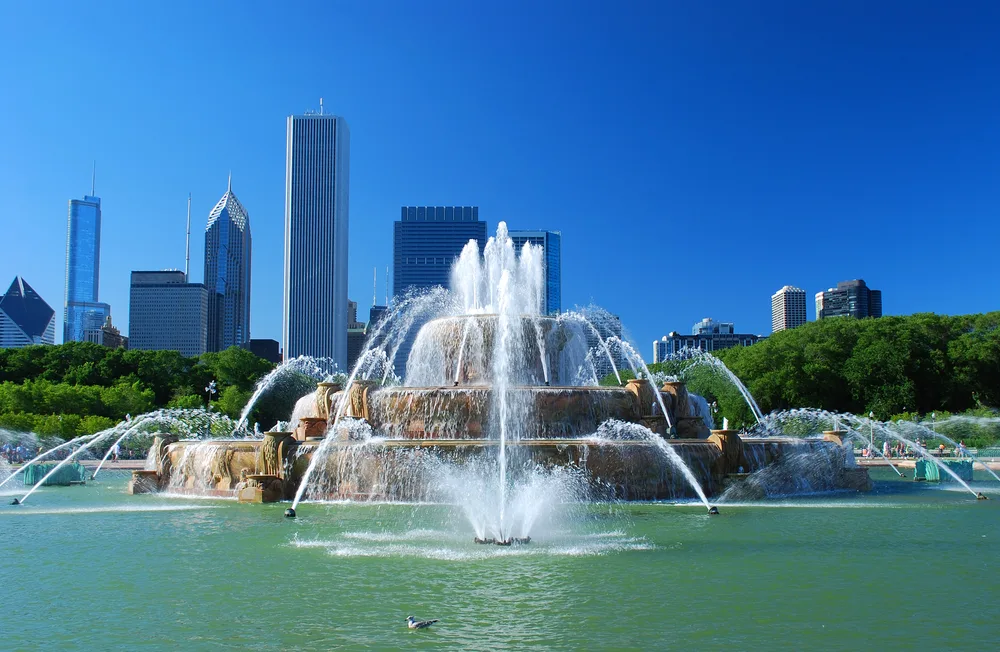 Featured as one of the best places to visit in Chicago, the Buckingham Fountain is pictured against a blue sky in the middle of Chicago