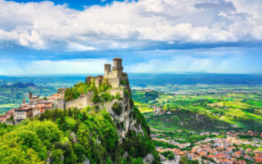 Guaita, the first tower of the Three Towers of San Marino, seen during the best time to visit San Marino with clouds and blue sky overhead with green hills all around