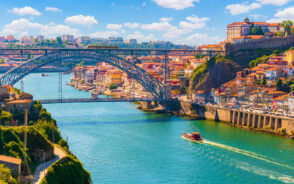 Aerial view of Old Town Porto with the Dom Luis Bridge crossing the Douro River as a boat moves under it during the best time to visit Porto in summer