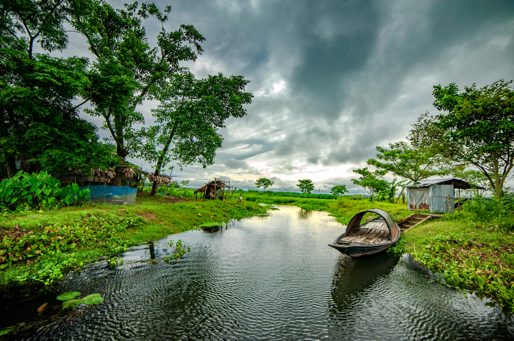 A traditional boat floats on the bank of the river during the monsoon season, the worst time to visit Bangladesh, with cloudy skies overhead