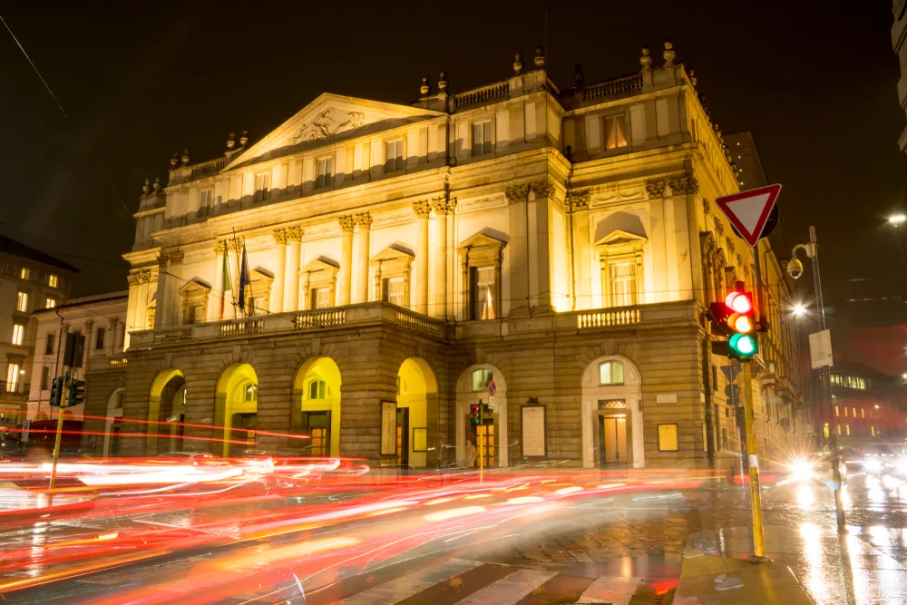 Teatro Alla Scala opera image taken at night with light trails in front of it indicate the cheapest time to visit Milan from November to January in the winter