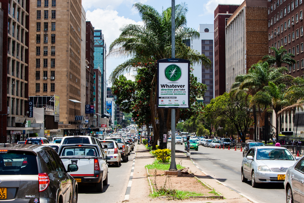 Busy street in Harare, Zimbabwe, pictured with cars and trucks in a long line on either side of the palm-tree-lined median