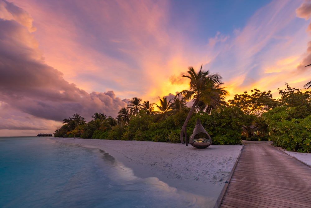 Sunset over the Maldives island with gorgeous rays of light protruding upward from the trees