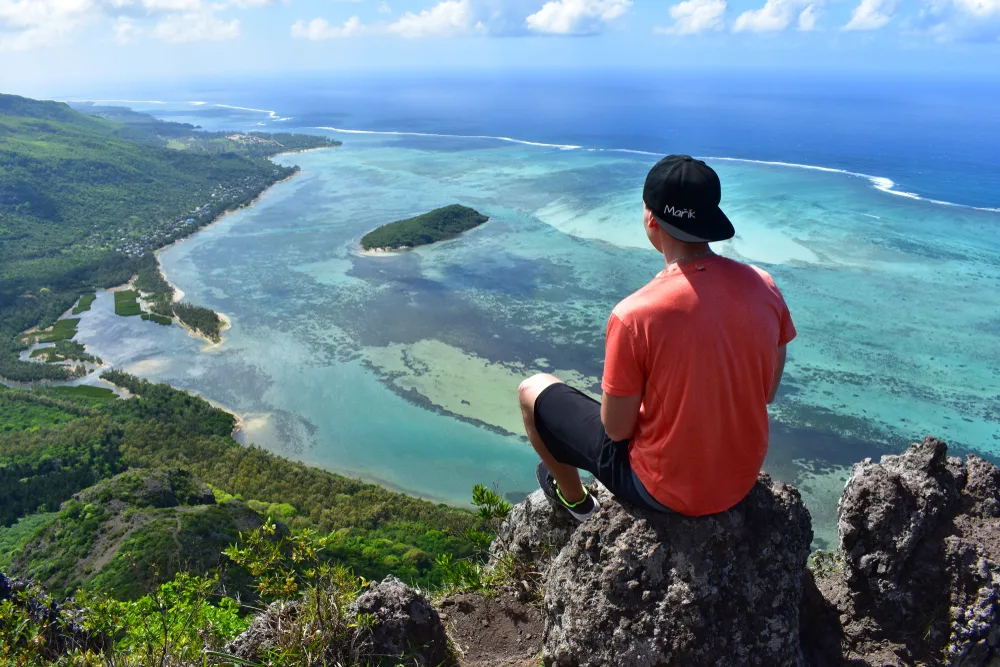 Guy sitting on a rock overlooking the expansive coastline below for a guide to whether or not Mauritius is safe to visit