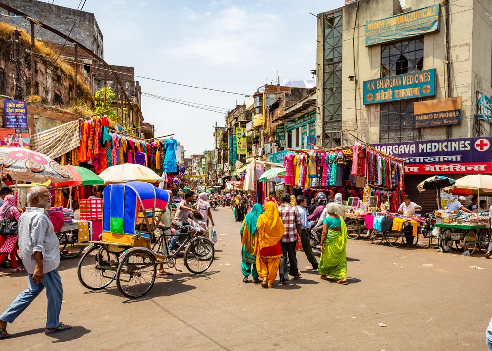 Chaotic traffic in an open-air market in New Delhi pictured on a clear day with carts and people in colorful clothes making their way down the street