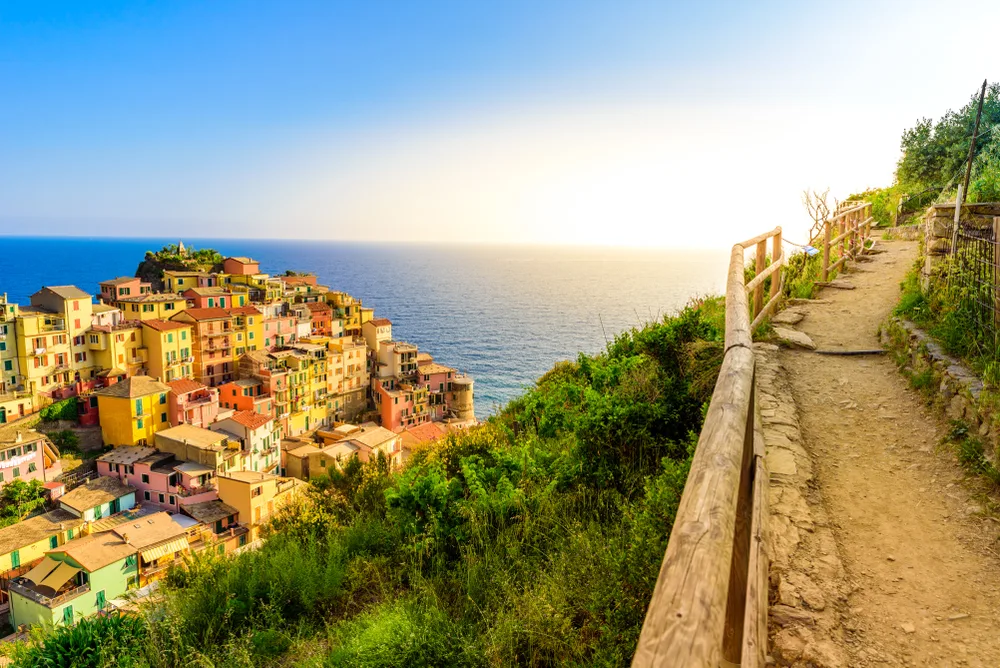 Hiking trail winds around the hill overlooking Manarola village on a clear day during the best time to visit Cinque Terre