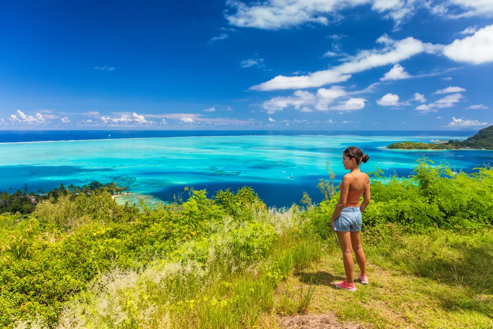 Petite asian tourist pictured standing on a hilltop by herself soaking up the view to help illustrate whether or not Bora Bora is safe to visit