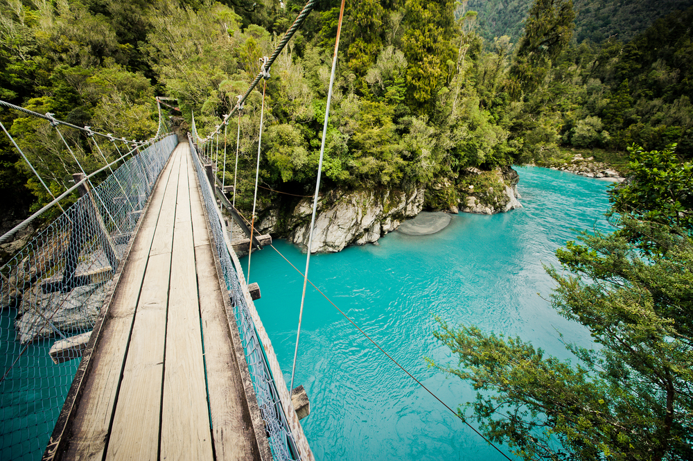 Picturesque view of a wooden bridge crossing teal water in the Hokitika Gorge in New Zealand