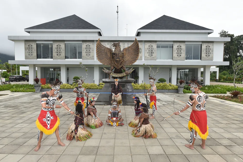 Tribal people in traditional clothing pictured in front of a government building pictured for a section on unsafe places to avoid in Indonesia