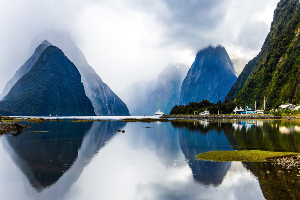 Clouds over Milford Sound pictured with fog rolling in by the mountains with white sky overhead