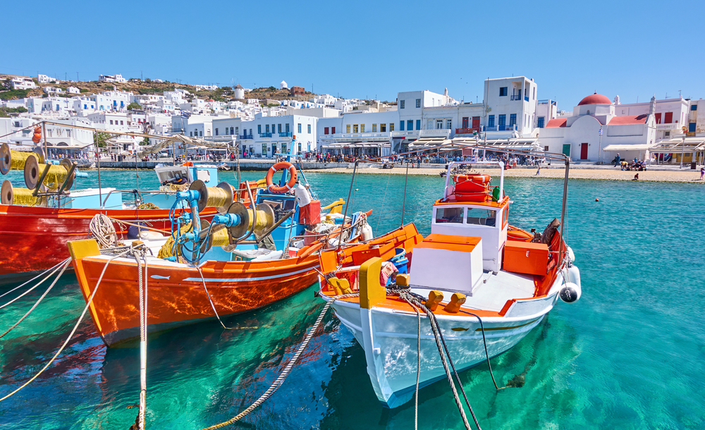 Wooden fishing boats wait in the harbor in the Old Town area during the best time to visit Mykonos with blue skies overhead