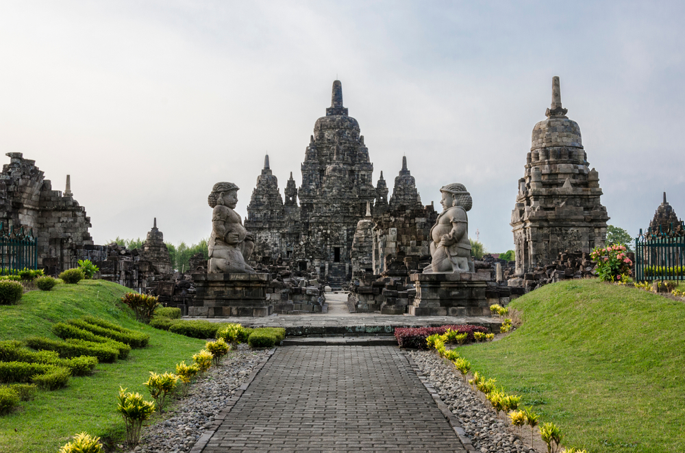 Photo of the outside of the Prambanan Temple pictured on a foggy day between two grassy berms