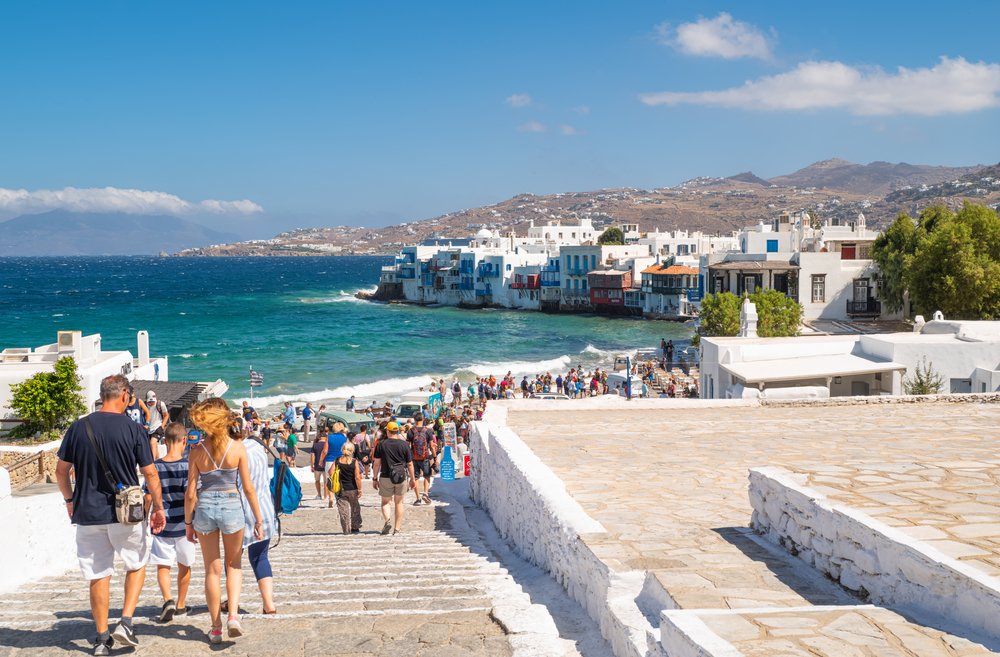 Big crowds of tourists enter Little Venice in Chora during the worst time to visit Mykonos in July and August when it's peak tourism season