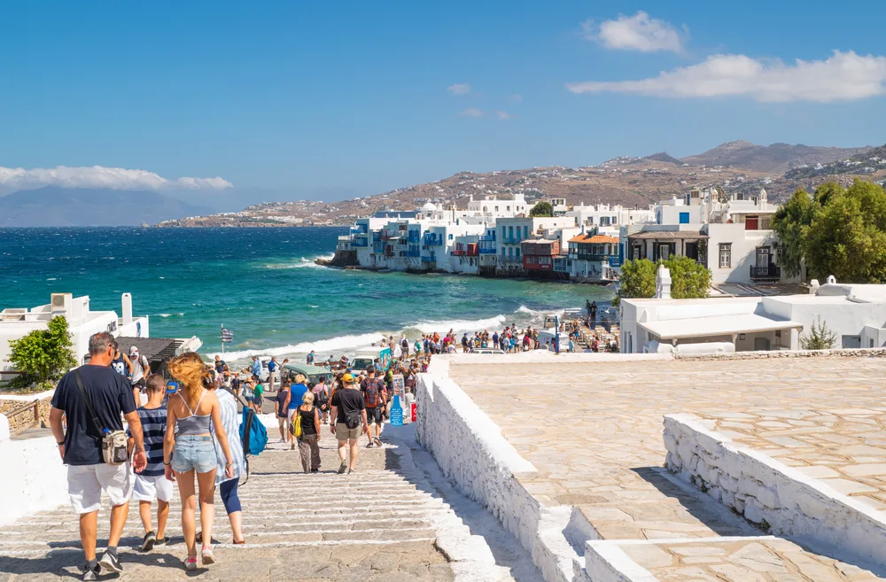 Big crowds of tourists enter Little Venice in Chora during the worst time to visit Mykonos in July and August when it's peak tourism season