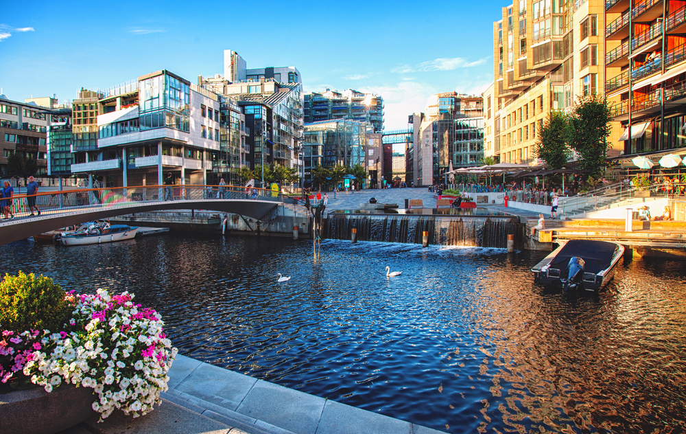 Neat view of the harbor in Oslo pictured during the overall best time to visit with boats floating on the water and flowers on either side of the canal