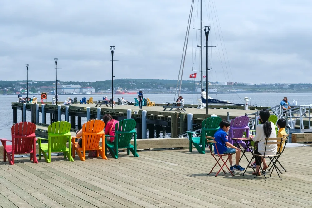 Two people sitting on a wooden boardwalk by the pier in Halifax during the overall best time to travel to Nova Scotia, Canada
