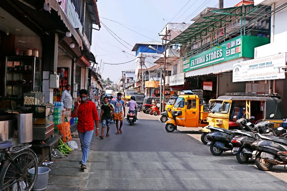 People walking along the street next to tuktuks and open-air shops with roll-up doors pictured for a guide to whether or not Kerala is safe to visit