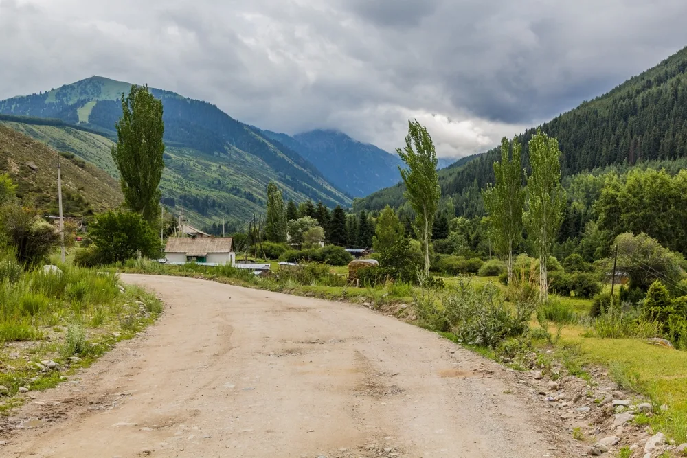 Road and village in a picturesque scene with clouds over the trees for a piece titled Is Kyrgyzstan safe to visit