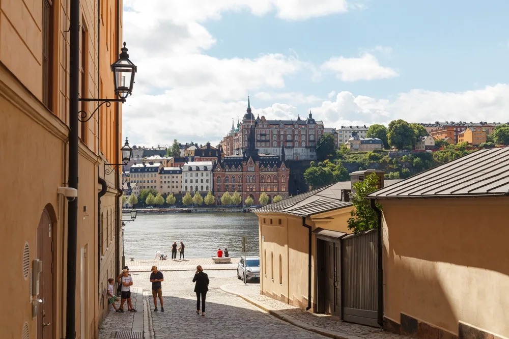 Two people walking along a brick street in the middle of buildings by a river in Stockholm for a piece on the best time to visit Scandinavia